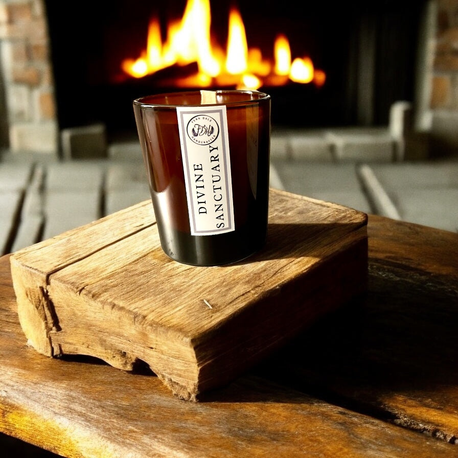 Divine Sanctuary candle in an amber glass jar on a rustic wooden block in front of a glowing fireplace.