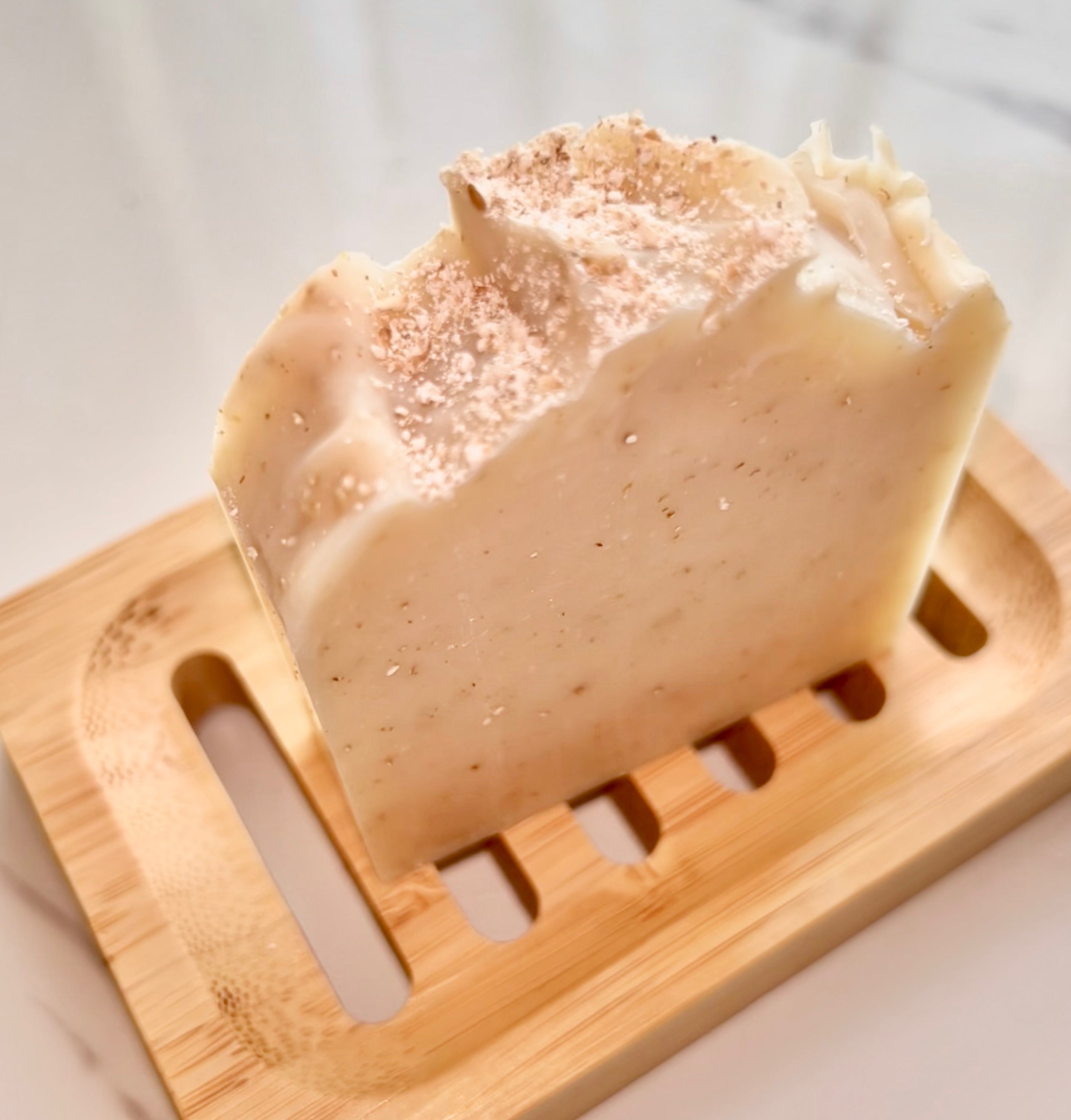 Oat & Shea Tallow Soap, a cream-coloured speckled bar with a textured top, on a slotted wooden soap dish.